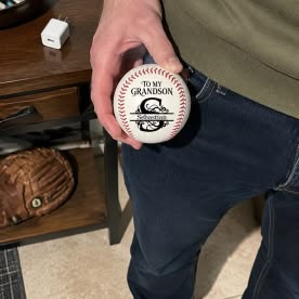 Customer photo of a hand holding a personalized baseball for his grandson Sebastian, with a baseball glove on the shelf behind